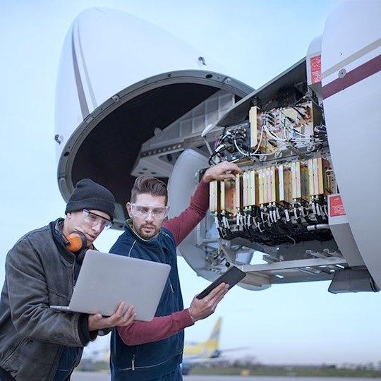 两名男性飞机技术人员在飞机机头工作，查看笔记本电脑上的信息
