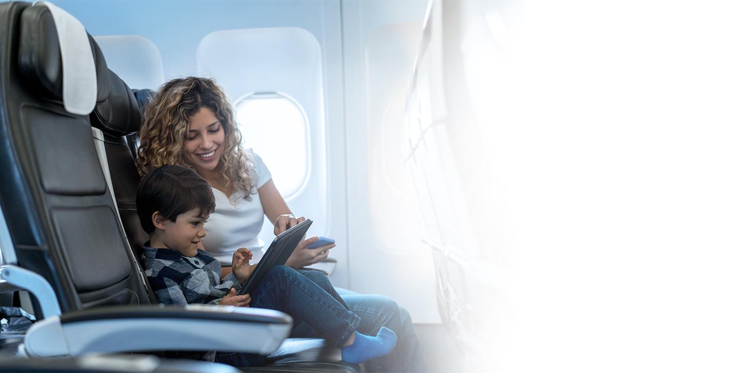A woman sitting next to her son on a plane is helping him connect his tablet to on-plane wifi